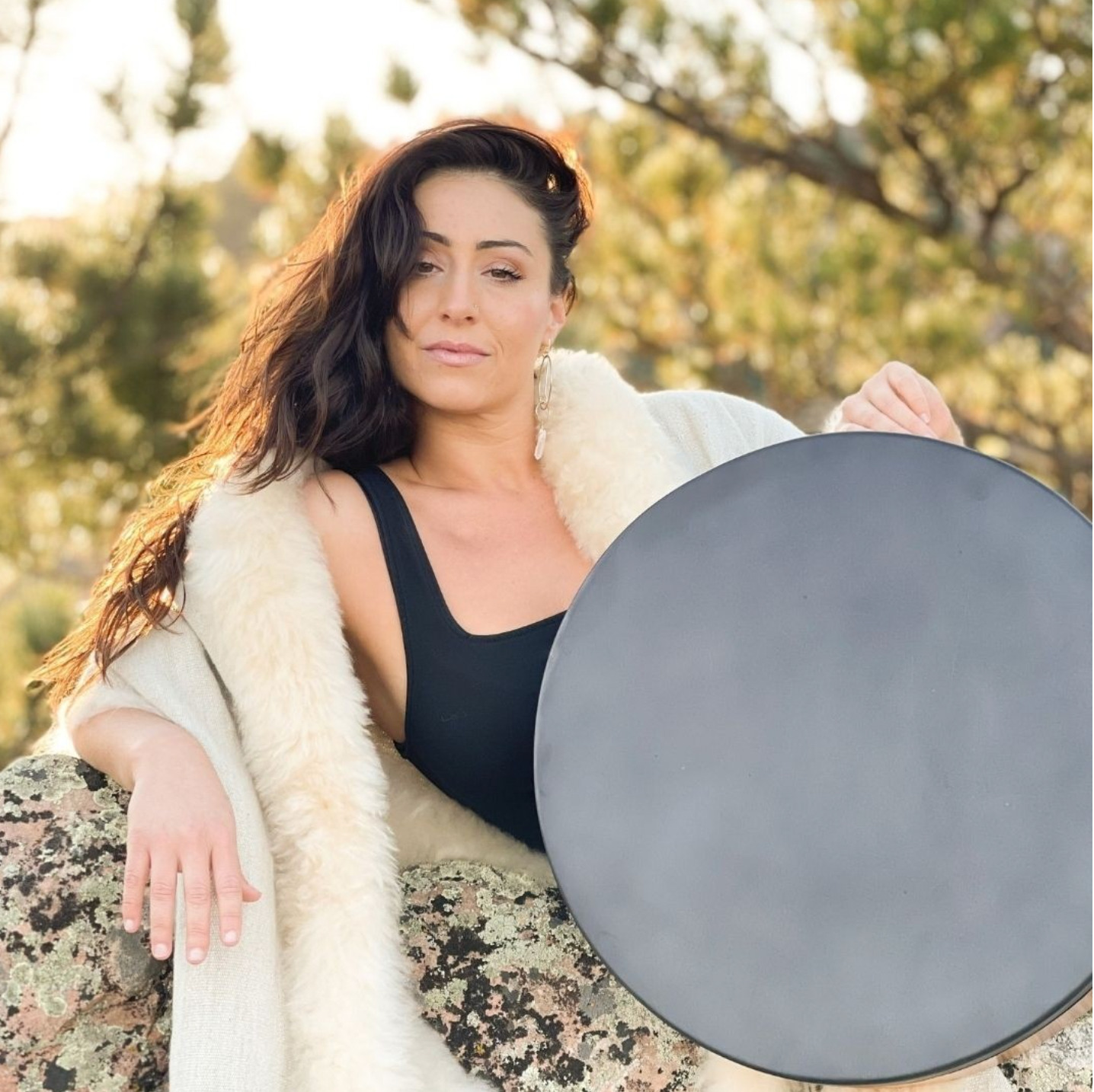 Larisa Gosla seated outdoors with a frame drum